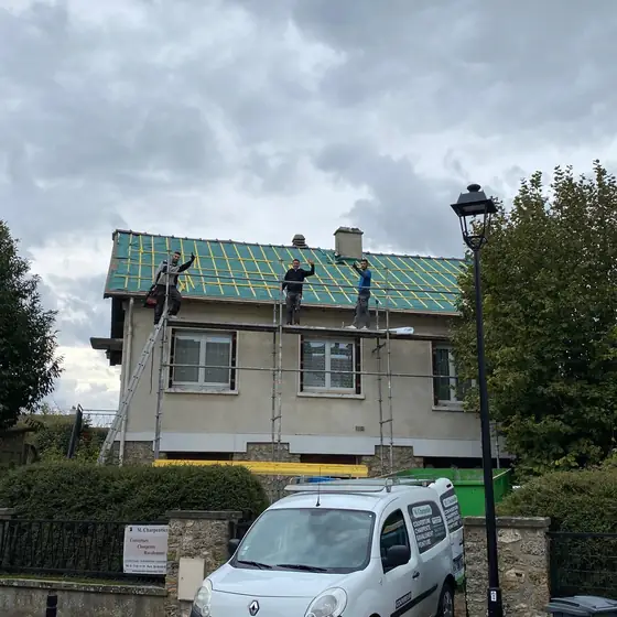 L'équipe de M. Charpentier sur la toiture d'un pavillon en cours de rénovation, camionnette de l'entreprise devant la maison